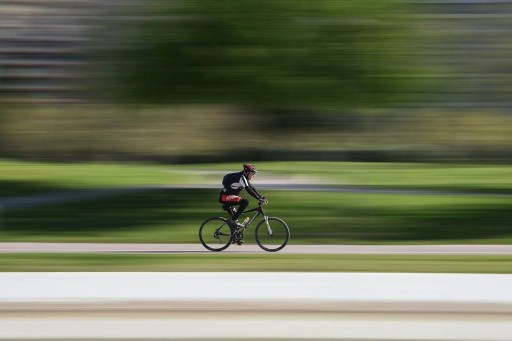 Unterwegs mit dem Rennrad Prostatahilfe Deutschland: Ein Rennradfahrer fährt auf einem Radweg, vor einem grünen Hintergrund (Tiefenunschärfe).